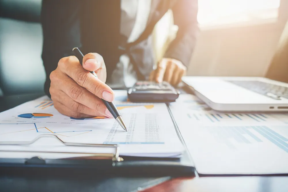 Una persona firma documentos con gráficos financieros junto a una calculadora